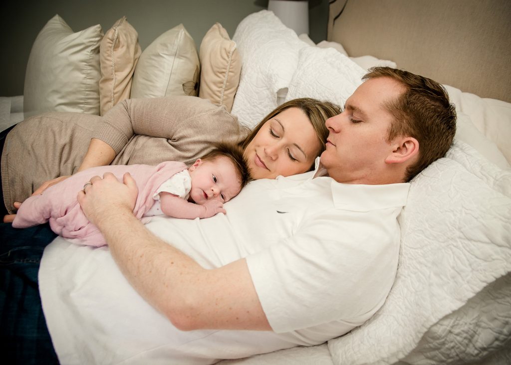 Mom and Dad lying on bed resting with newborn on Dad's tummy