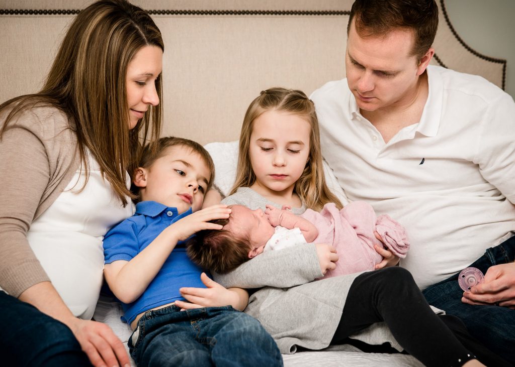 older sister holding newborn surrounded by Mom, Dad and brother
