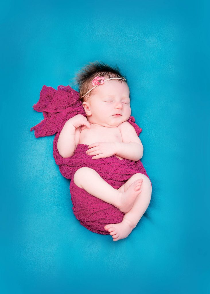 newborn sleeping wrapped in burgandy and lying on teal background