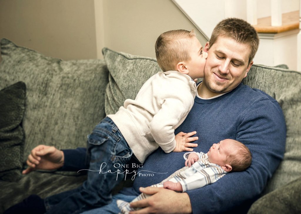4 year old boy kissing Dad on cheek with Newborn brother looking on