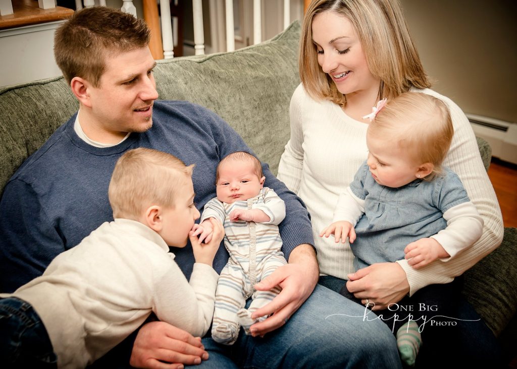 Mom, Dad and 2 kids welcome their new baby brother sitting on a green couch