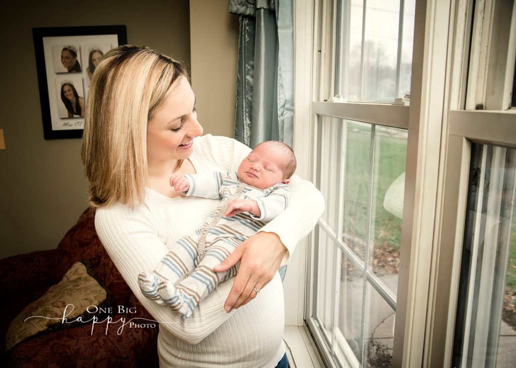 Mom holding newborn son by a window smiling down at him