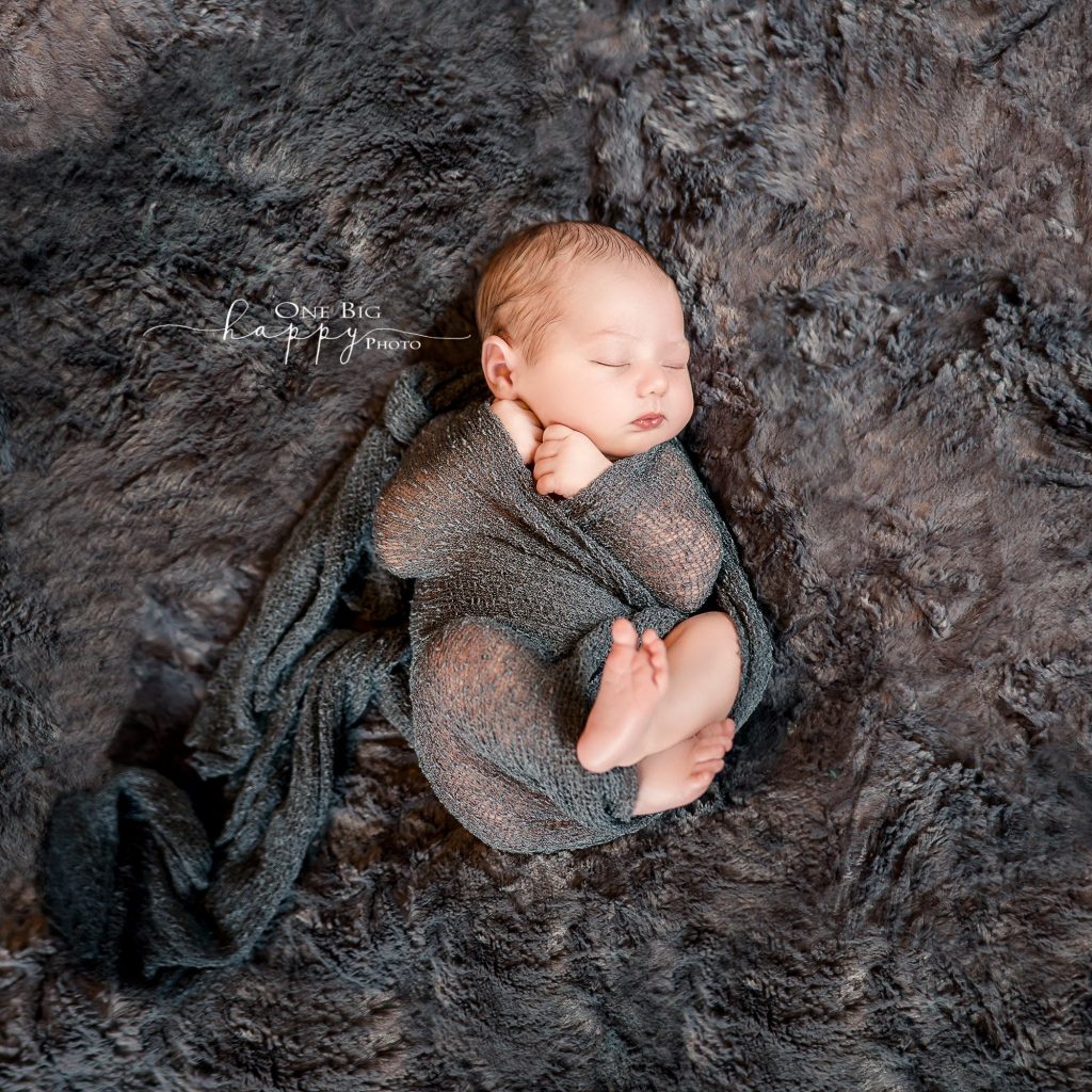 newborn baby boy wrapped in grey scarf lying on grey fur blanket