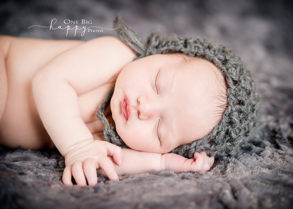 Newborn baby boy sleeping in grey knit cap on grey blanket