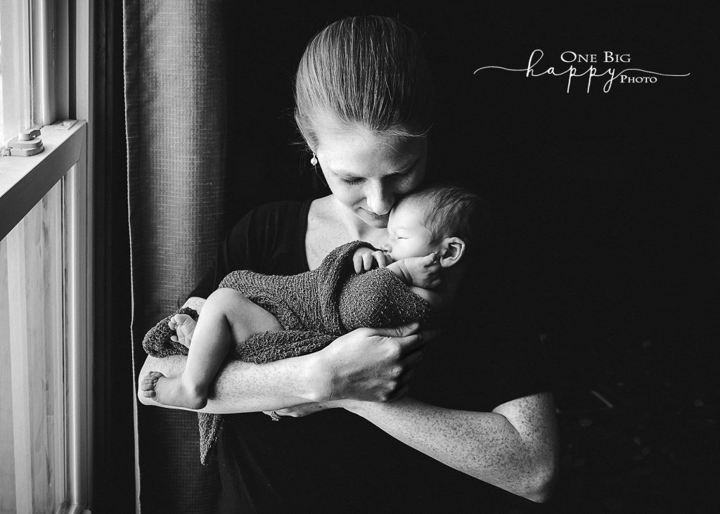 black and white image of mom holding newborn son in window light