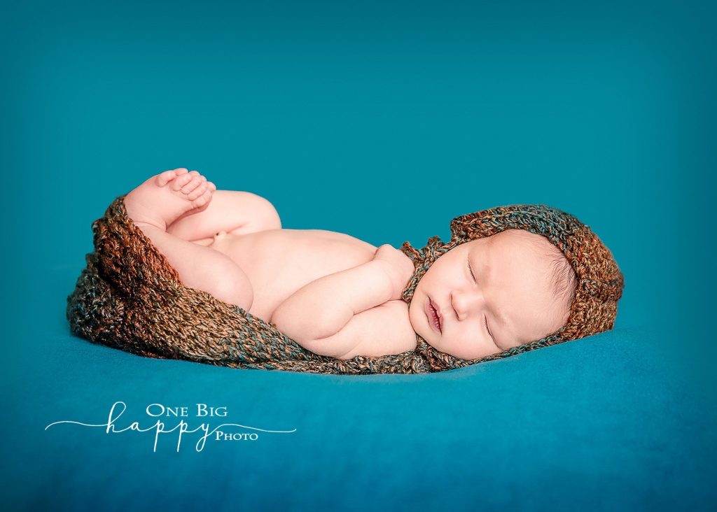 newborn boy wrapped in knit lying on his back on blue blanket