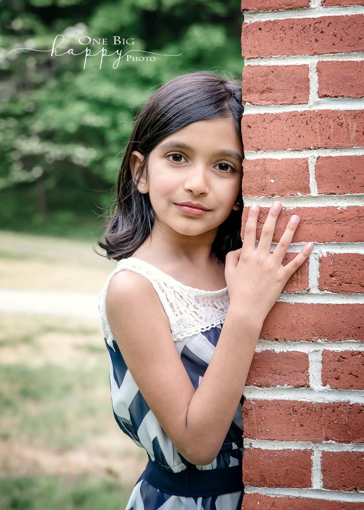 Young Indian girl poses for serious summer portrait against brick wall