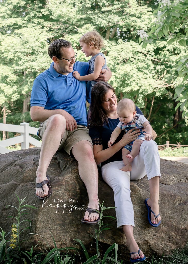 Family of 4 sitting on a bolder in front yard for portrait in summer