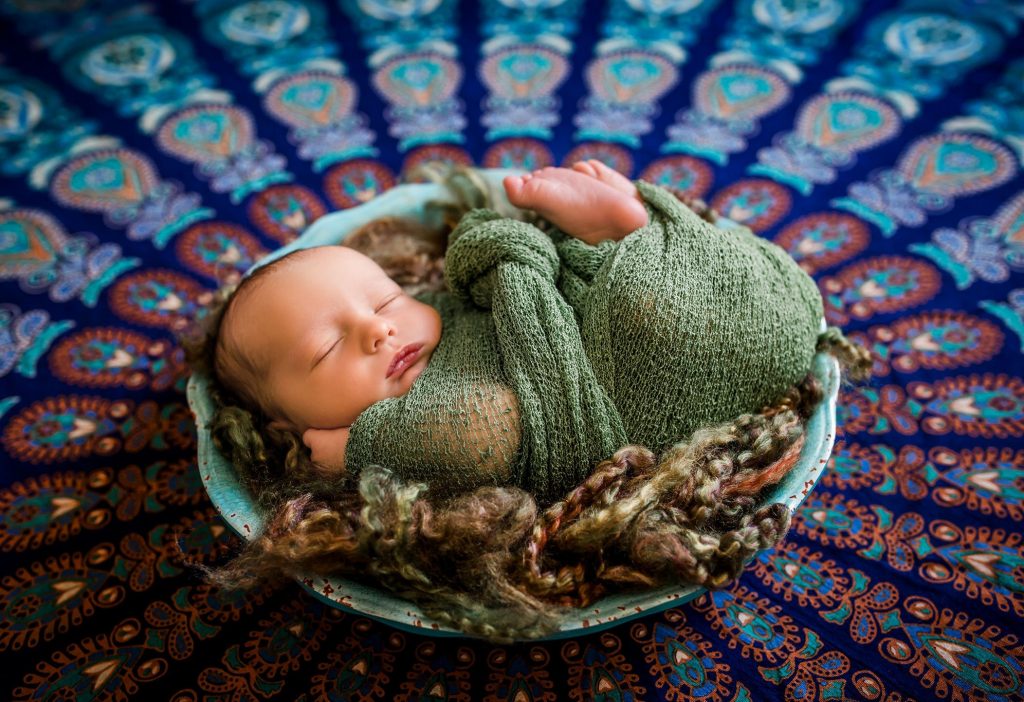 newborn baby curled up in a bowl with green wrap on colorful background Glastonbury CT Newborn Photographer One Big Happy Photo www.onebighappyphoto.com/newborns