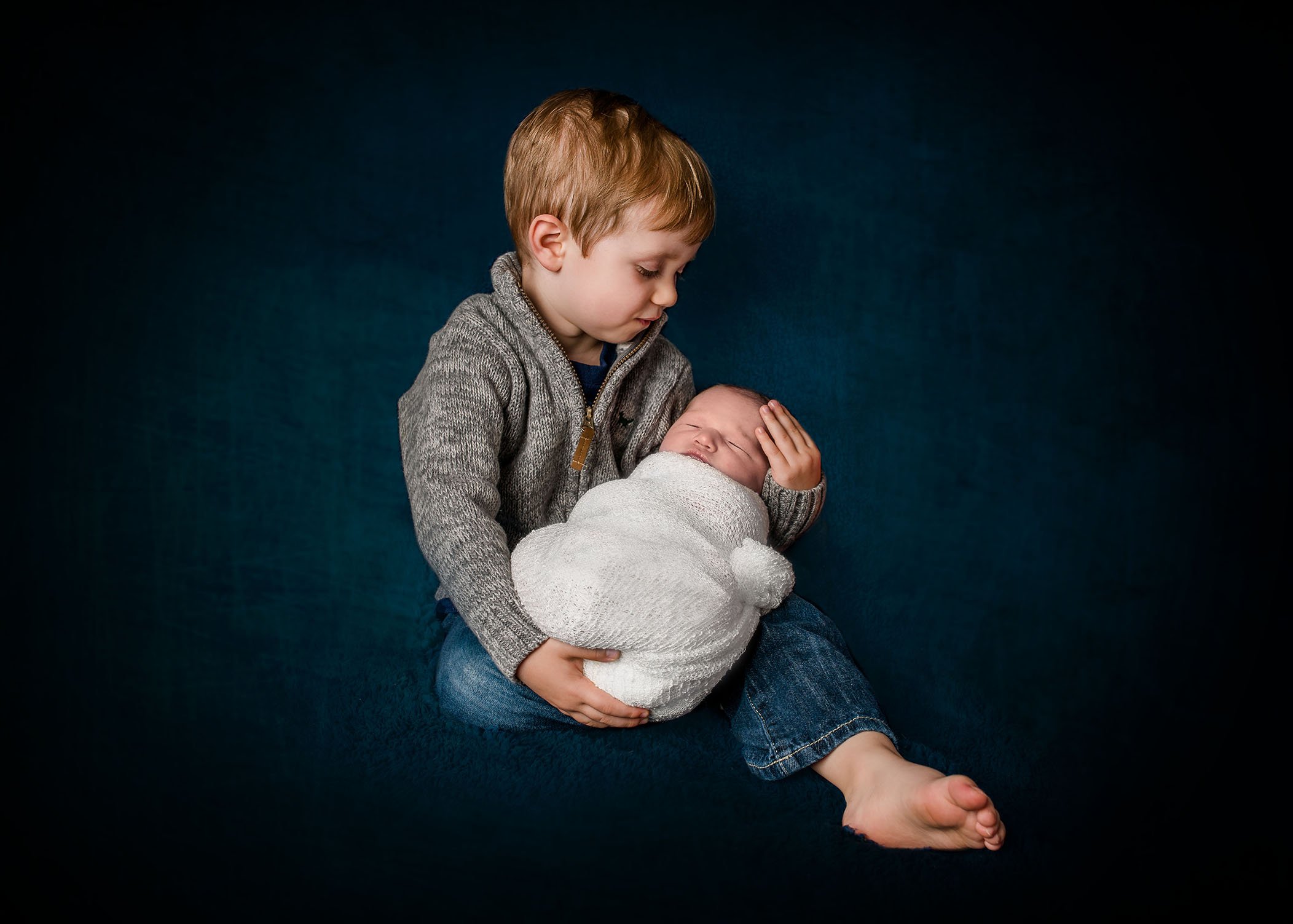 3 year old boy holding his newborn baby sister in his arms One Big Happy Photo
