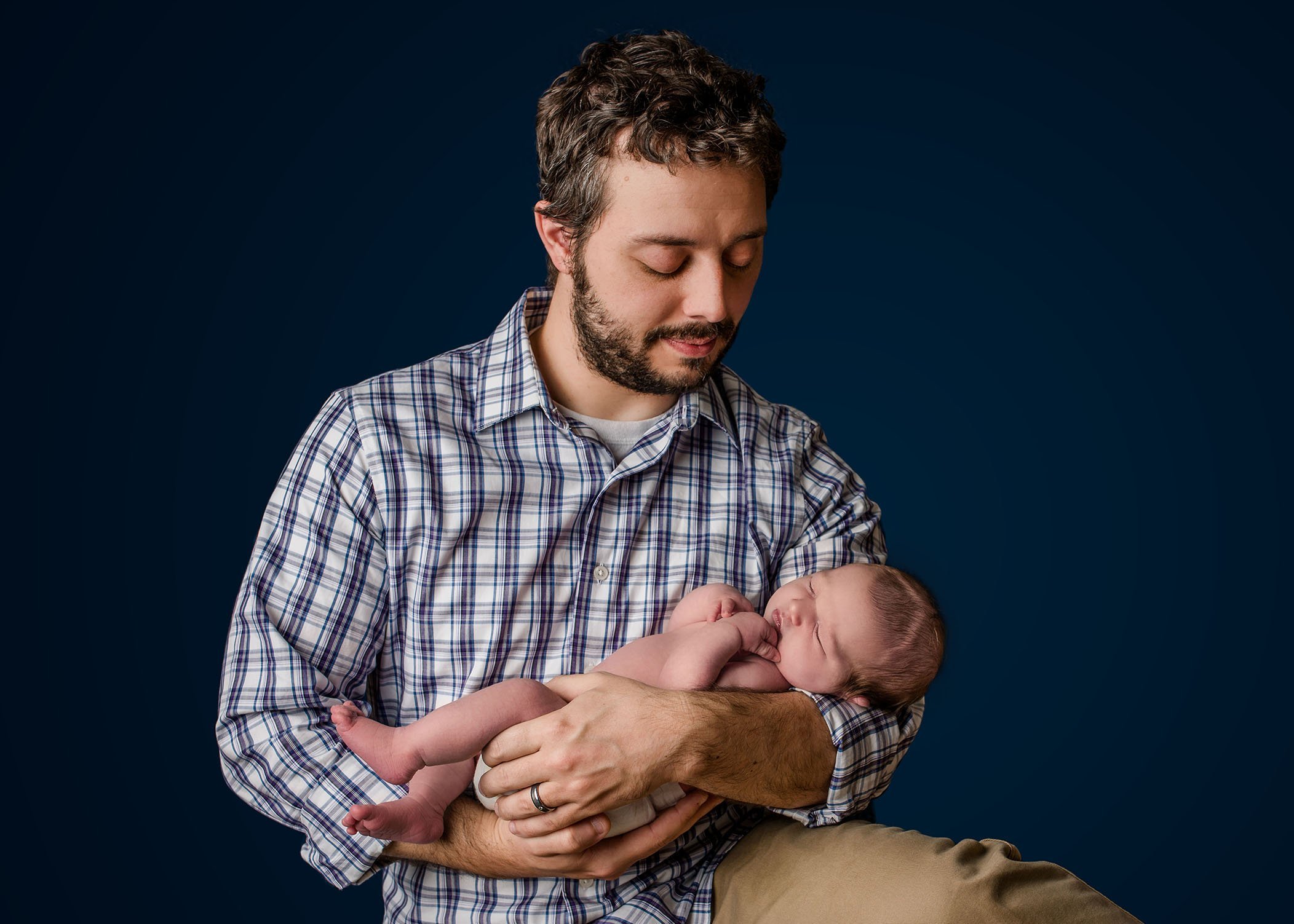 Dad holding newborn baby in his arms on blue One Big Happy Photo