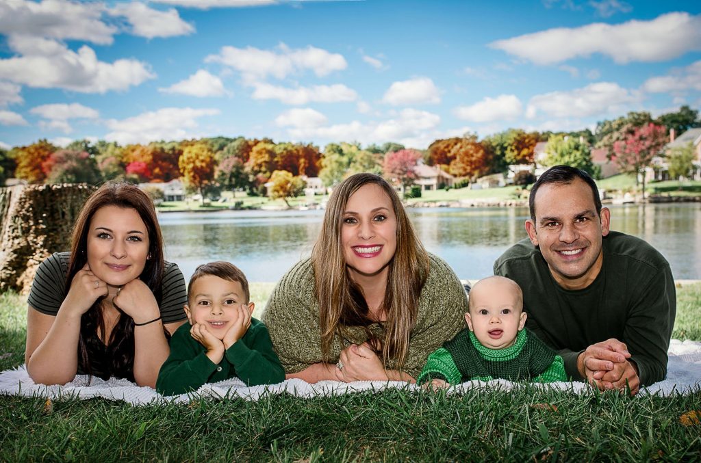 Family of 5 lying down on the grass on their elbows smiling for a family portrait One Big Happy Photo