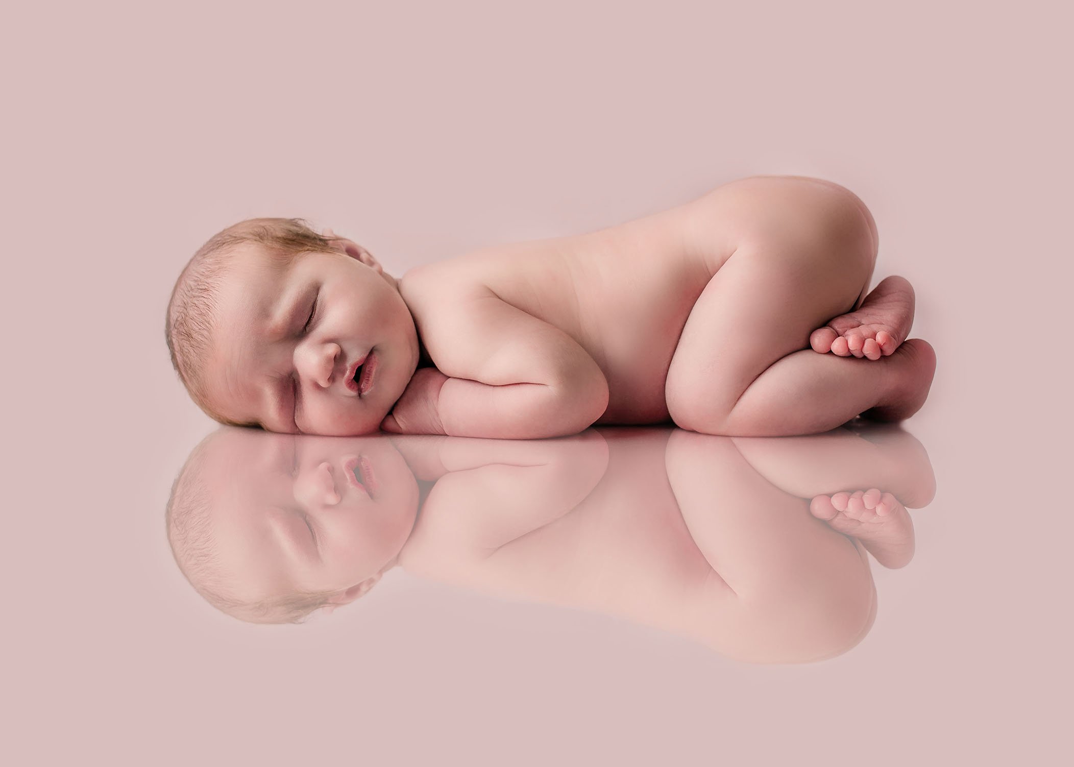 newborn baby girl lying on tummy on pink reflection One Big Happy Photo