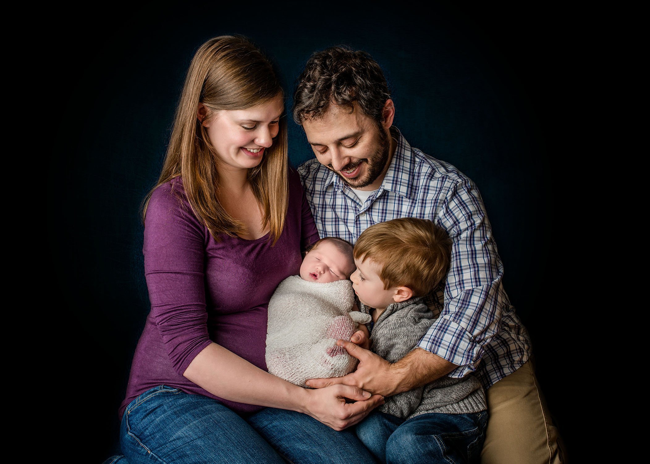newborn baby girl with her parents and big brother smiling down on her One Big Happy Photo
