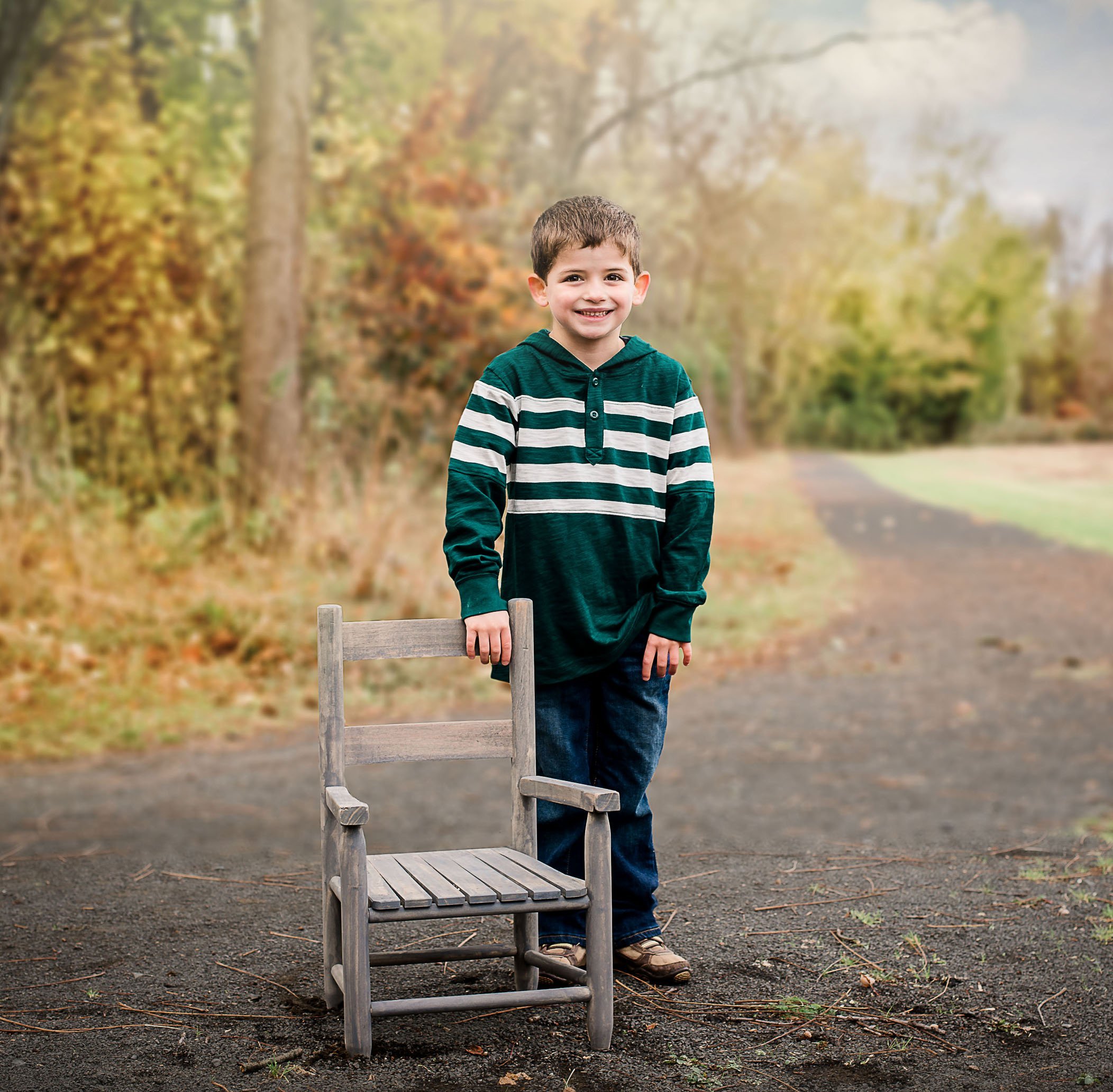 4 year old boy standing behind chair outside in fall