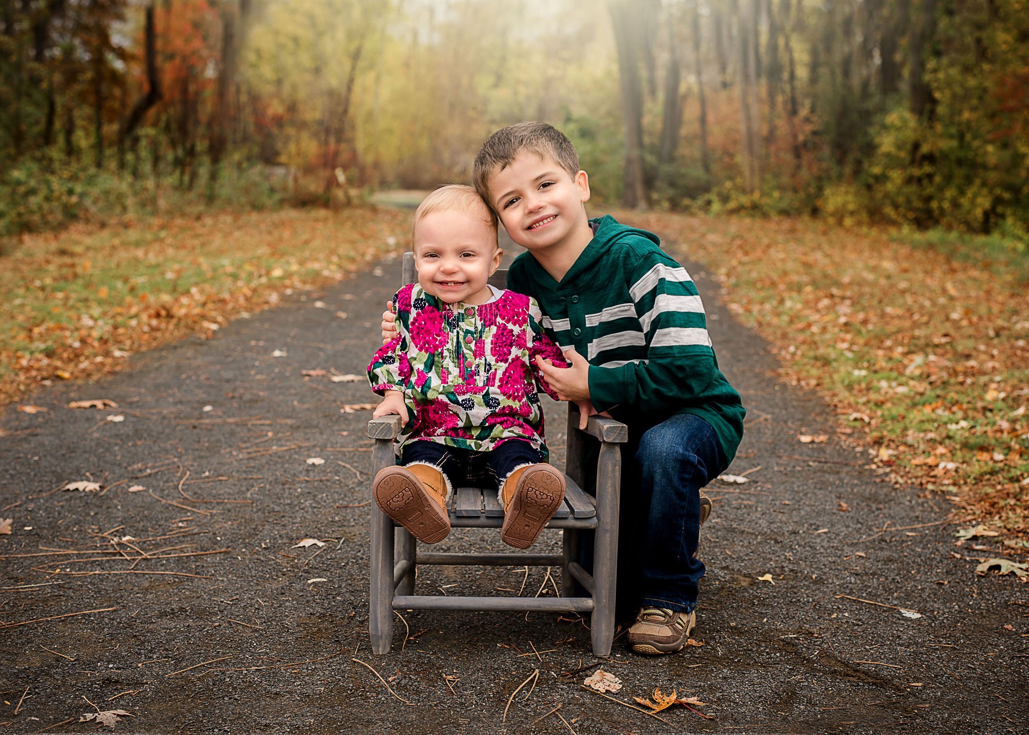 4 year old brother and 1 year old sister sitting in chair outside on path in Fall