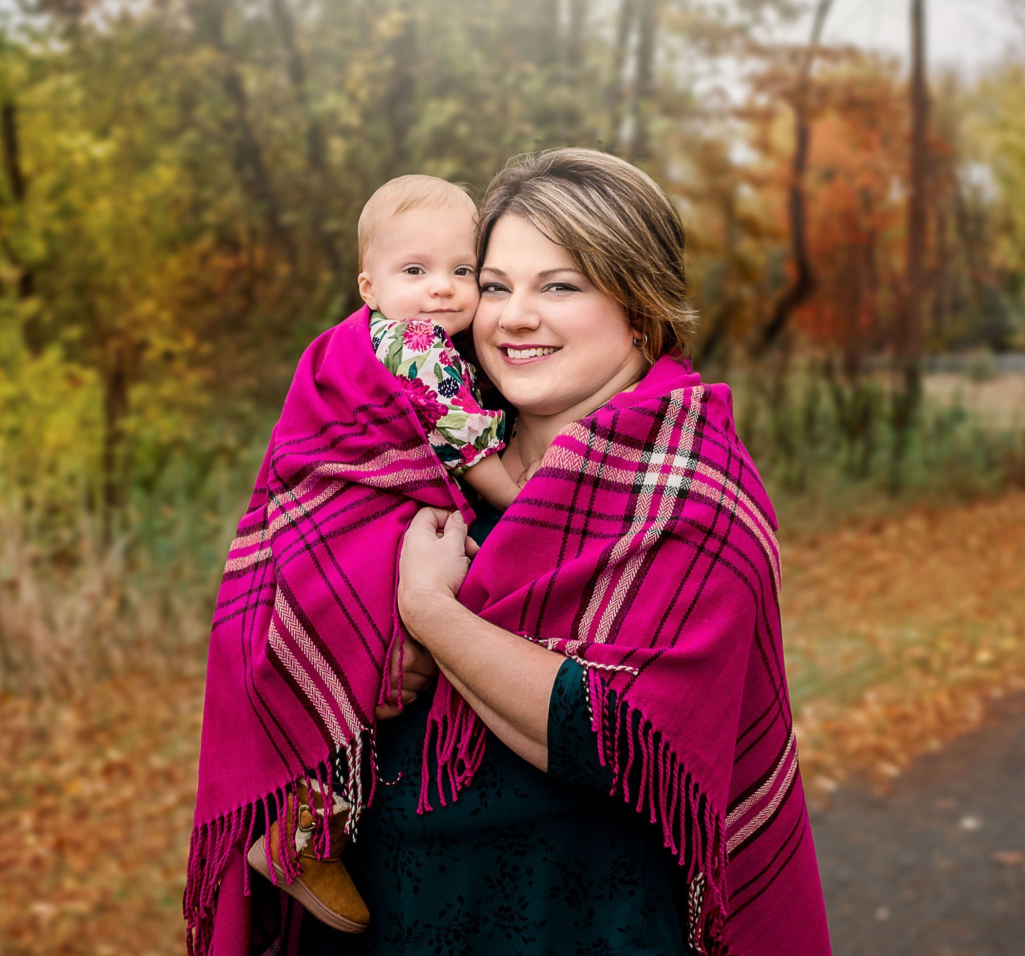 Mom snuggling her 1 year old daughter outside in fall under a bright pink blanket