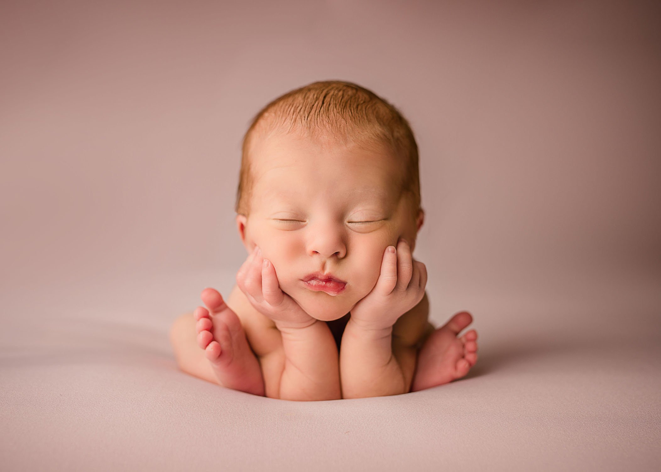 newborn girl posed in head in hands toes out front on pink