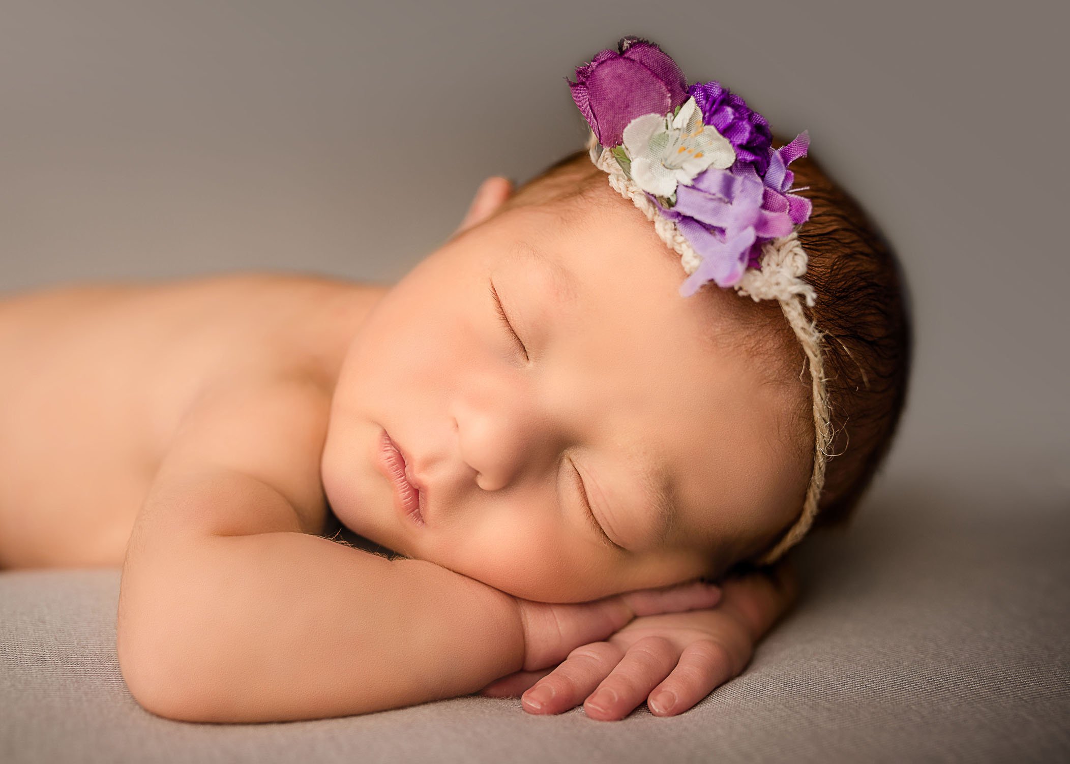newborn girl sleeping with head on hands wearing purple flower headband