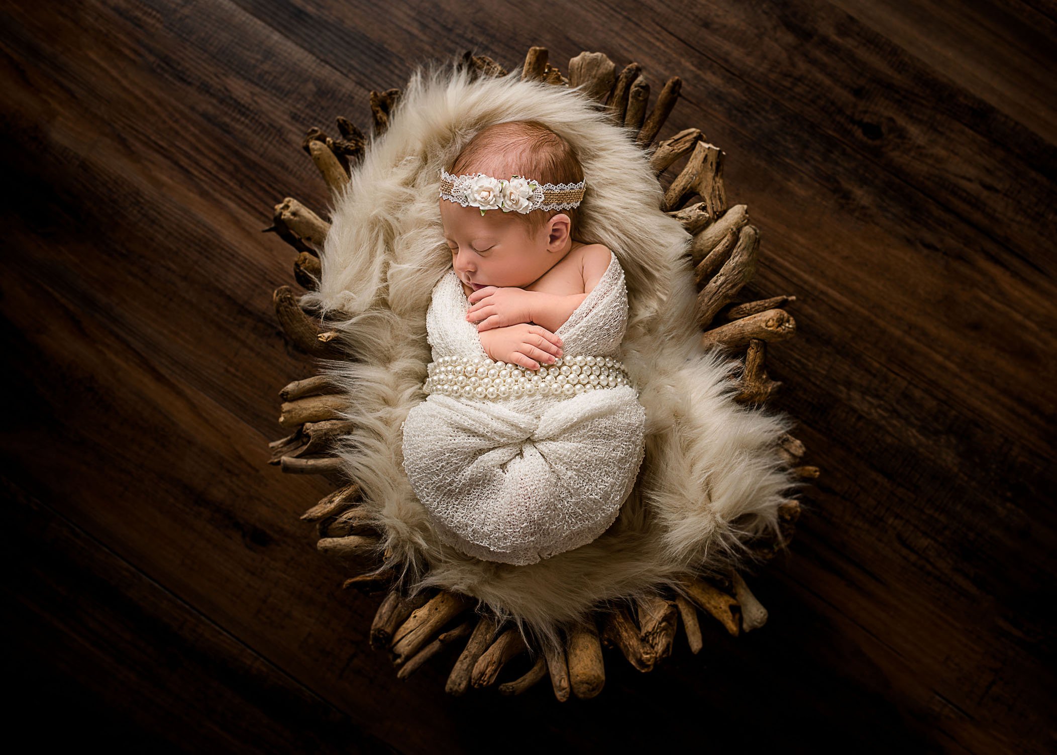 newborn baby sleeping swaddled in driftwood bowl and fur draped in long strands of pearls