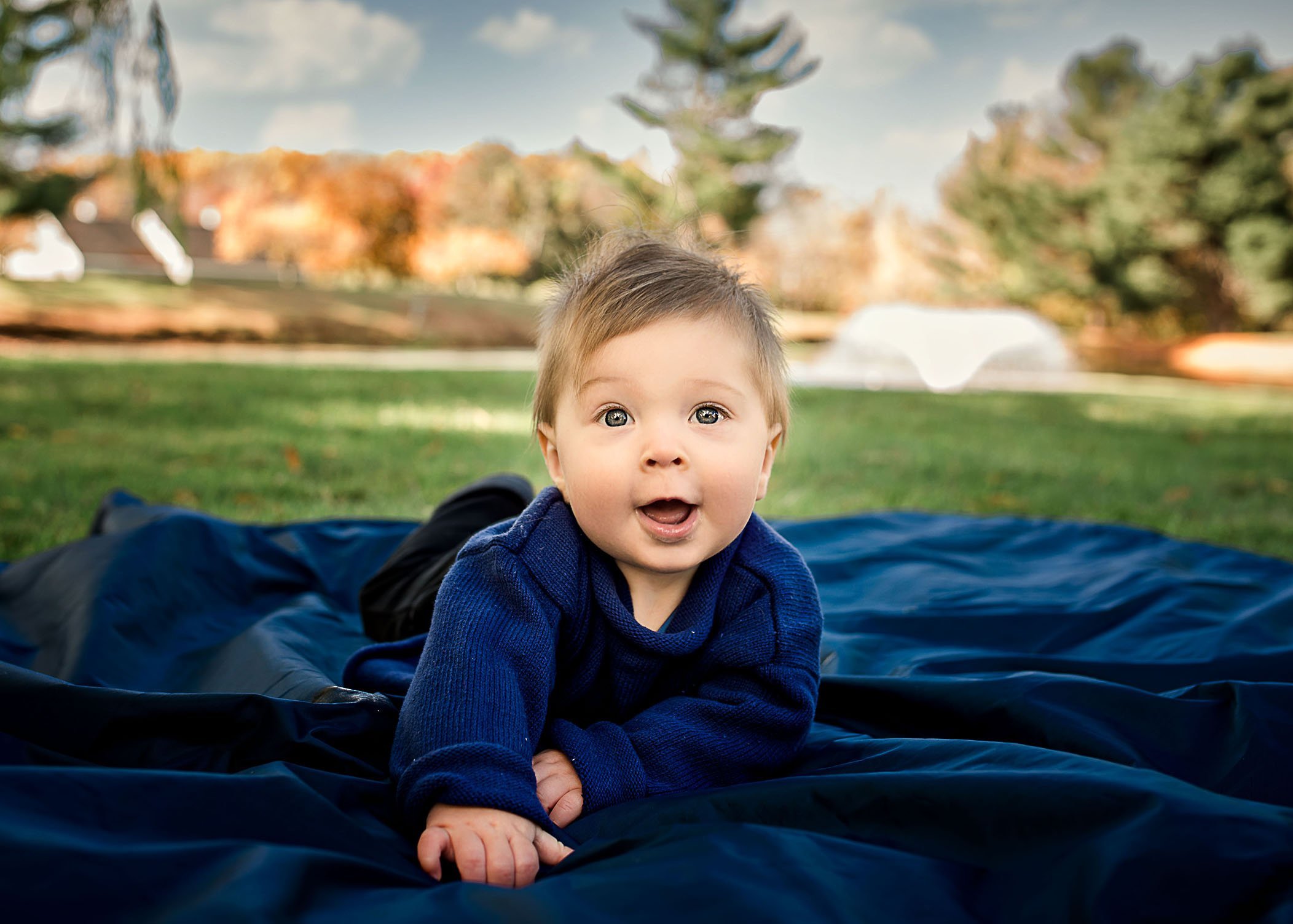 baby boy lying on blue blanket outside smiling One Big Happy Photo