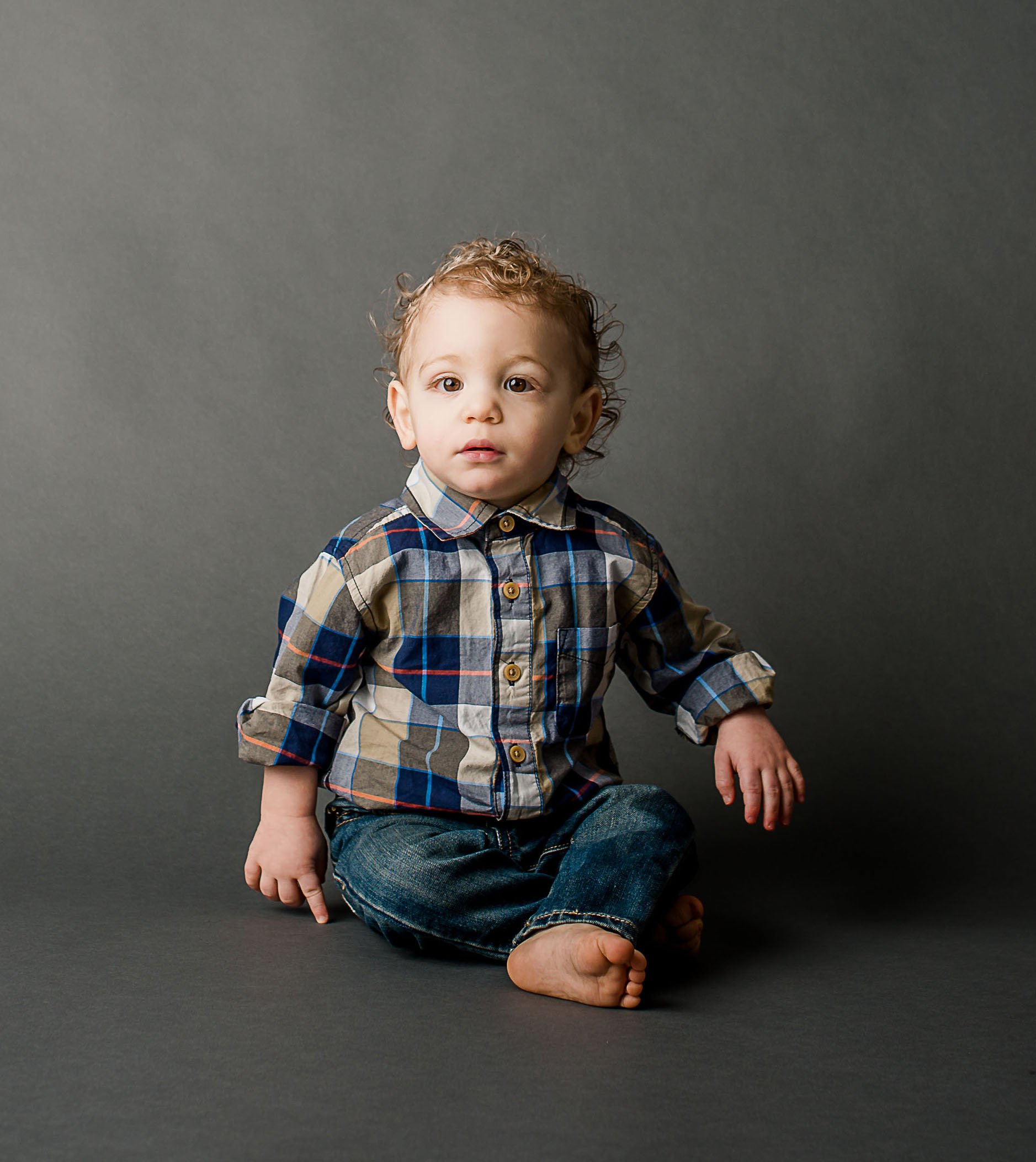 toddler boy sitting still in plaid shirt on grey background One Big Happy Photo