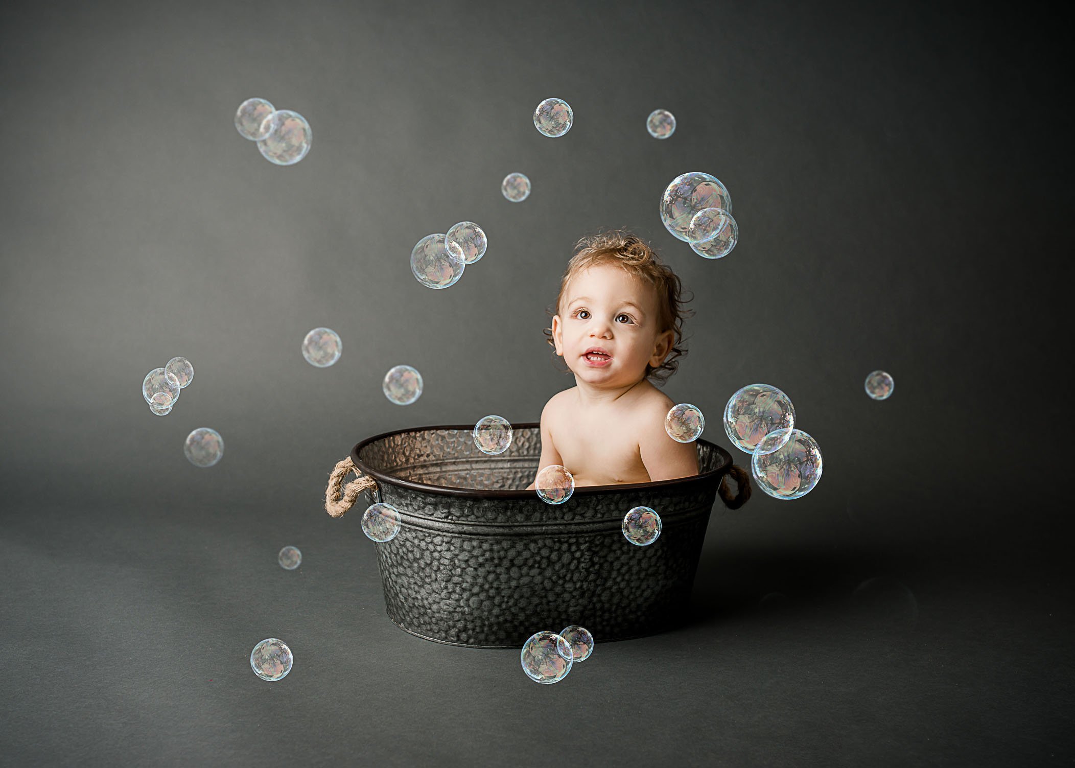 toddler sitting in tin bucket on grey background with colorful bubbles in air One Big Happy Photo