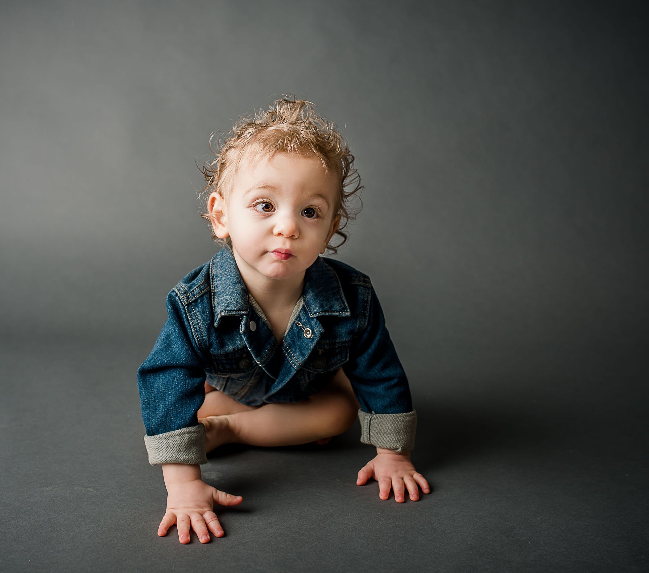 18 month old boy crawling on grey in a denim jacket One Big Happy Photo