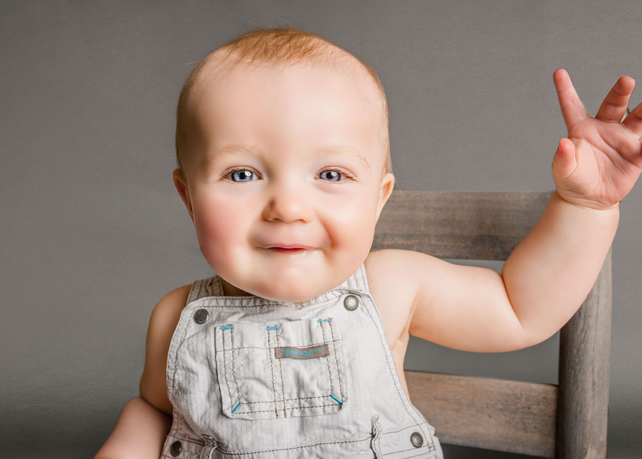 baby in overalls smiling with hand raised One Big Happy Photo