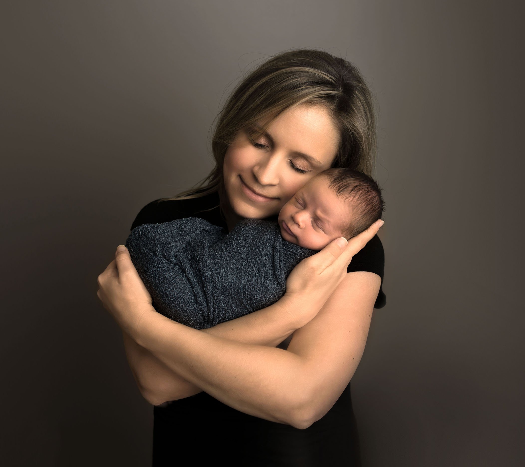 Mom cradles newborn in her arms with eyes closed and smile One Big Happy Photo