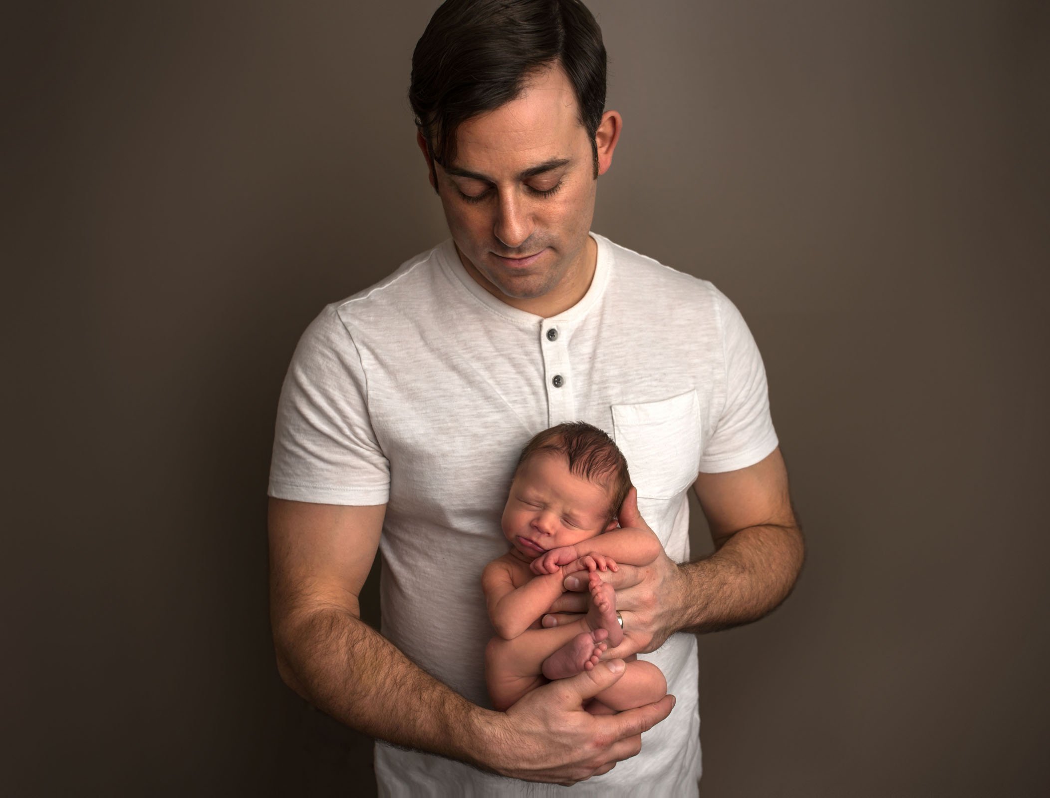 newborn held against dad's chest facing outward all curled up One Big Happy Photo