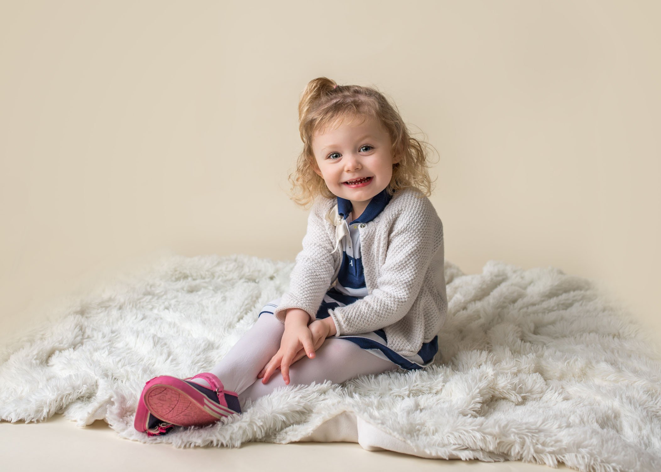 2 year old little girl sitting on white rug smiling One Big Happy Photo
