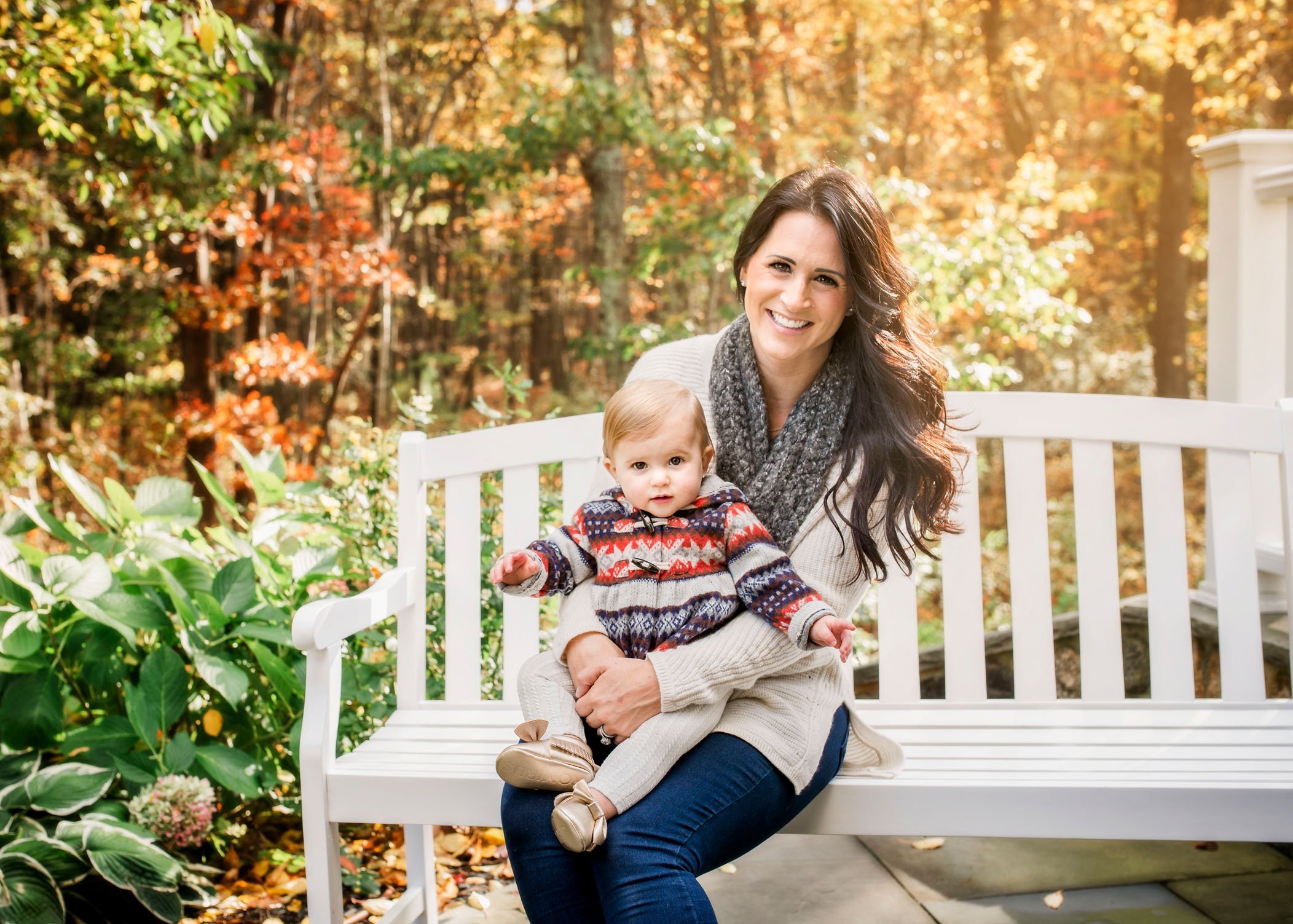 Mom holds 1 year old daughter on lap on bench outside in fall