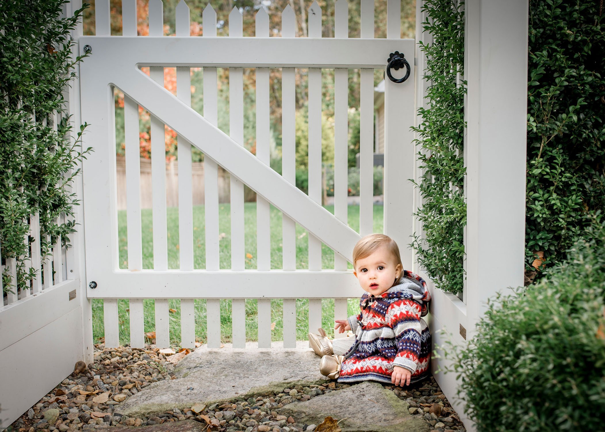 12 month old baby girl sits by backyard gate