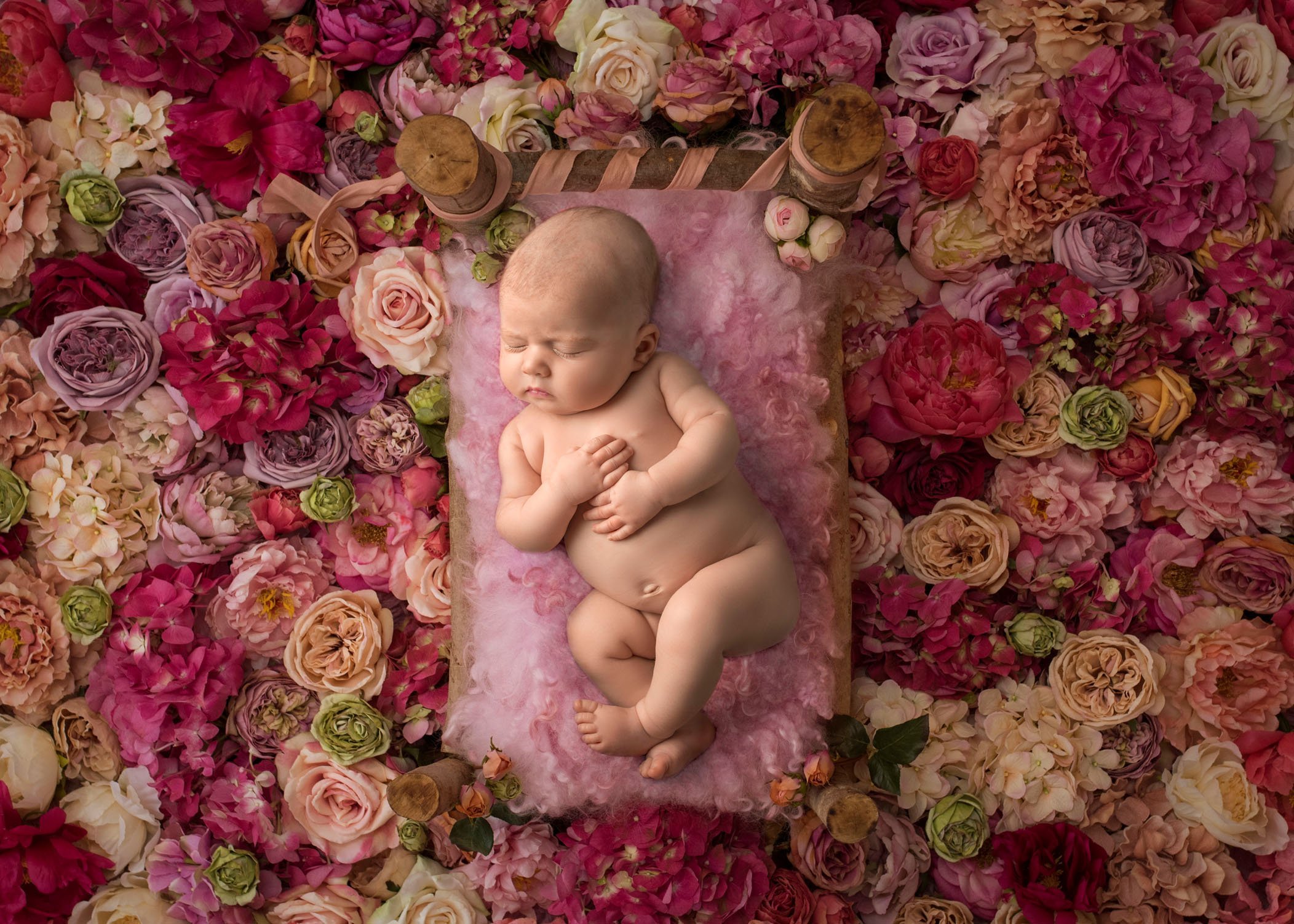 newborn baby girl sleeping on bed surrounded by colored roses
