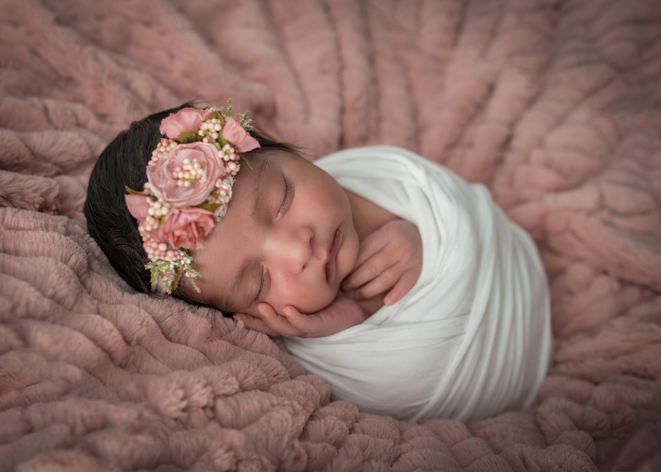 newborn baby sleeping on pink blanket with floral crown on head