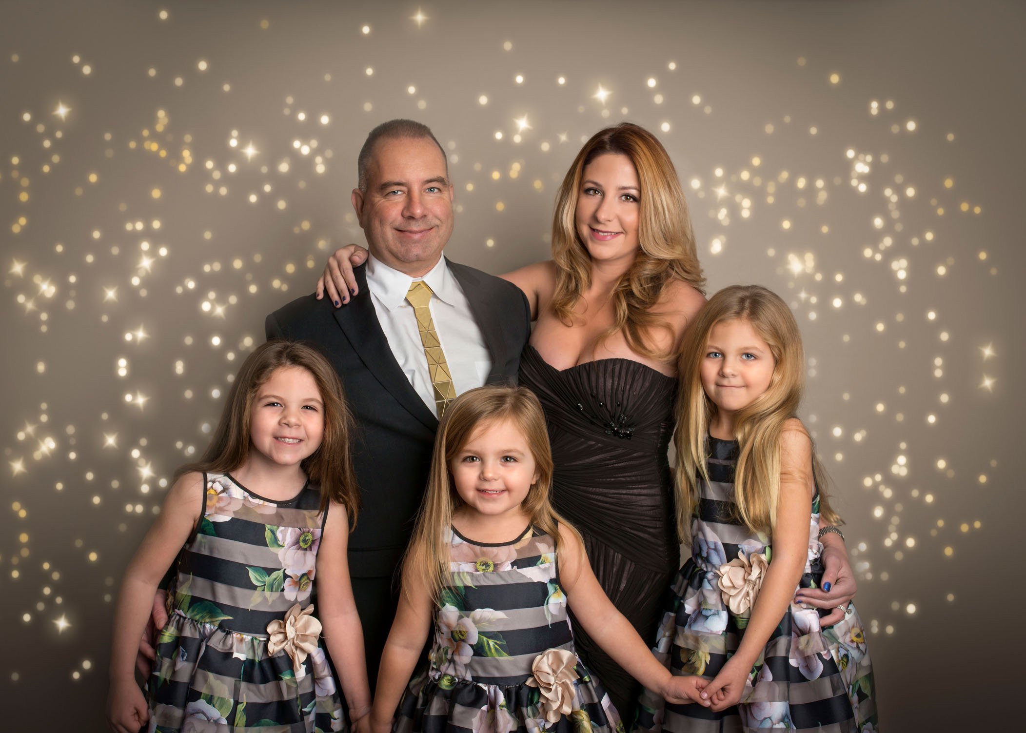 Family with 3 young daughters pose in front of bokeh backdrop