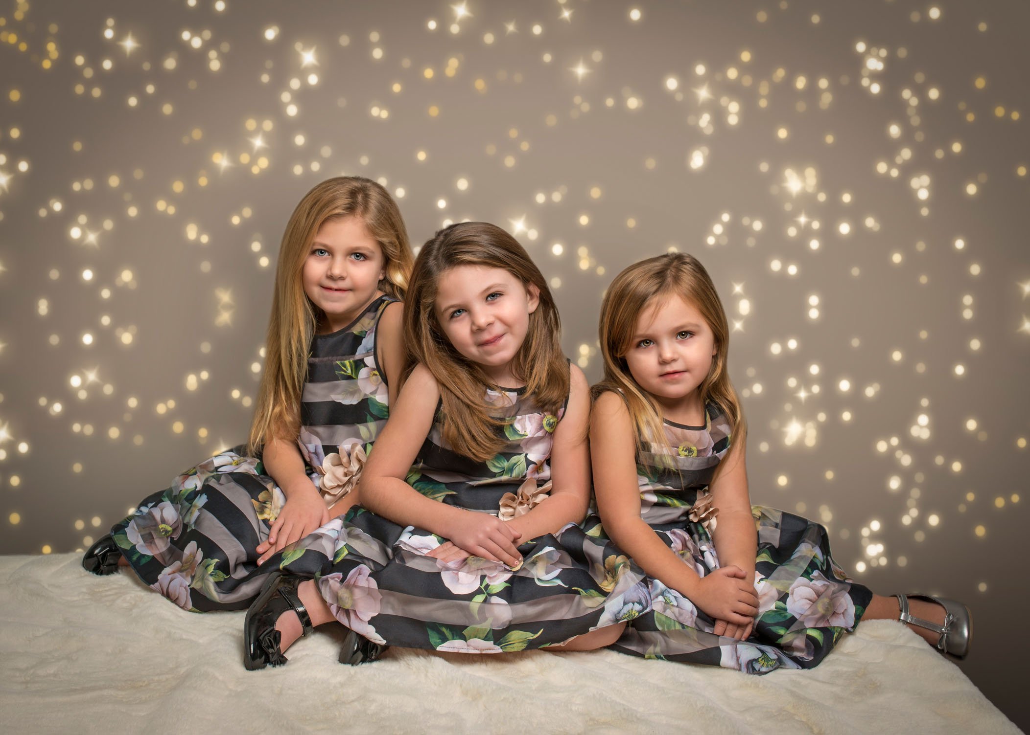 3 young sisters sitting in pretty dresses with bokeh lights behind them