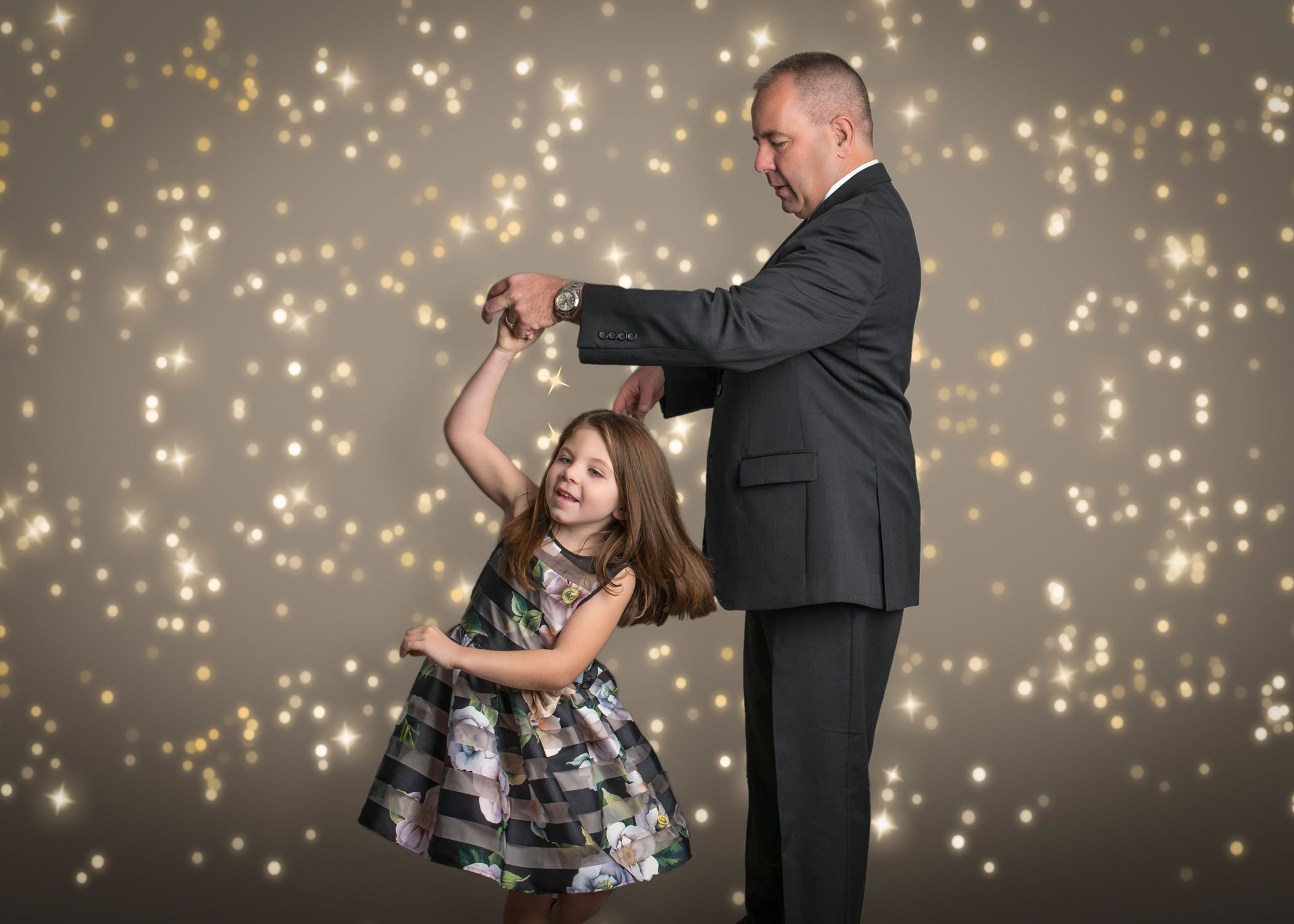 Dad twirling 5 year old daughter with bokeh lights behind them