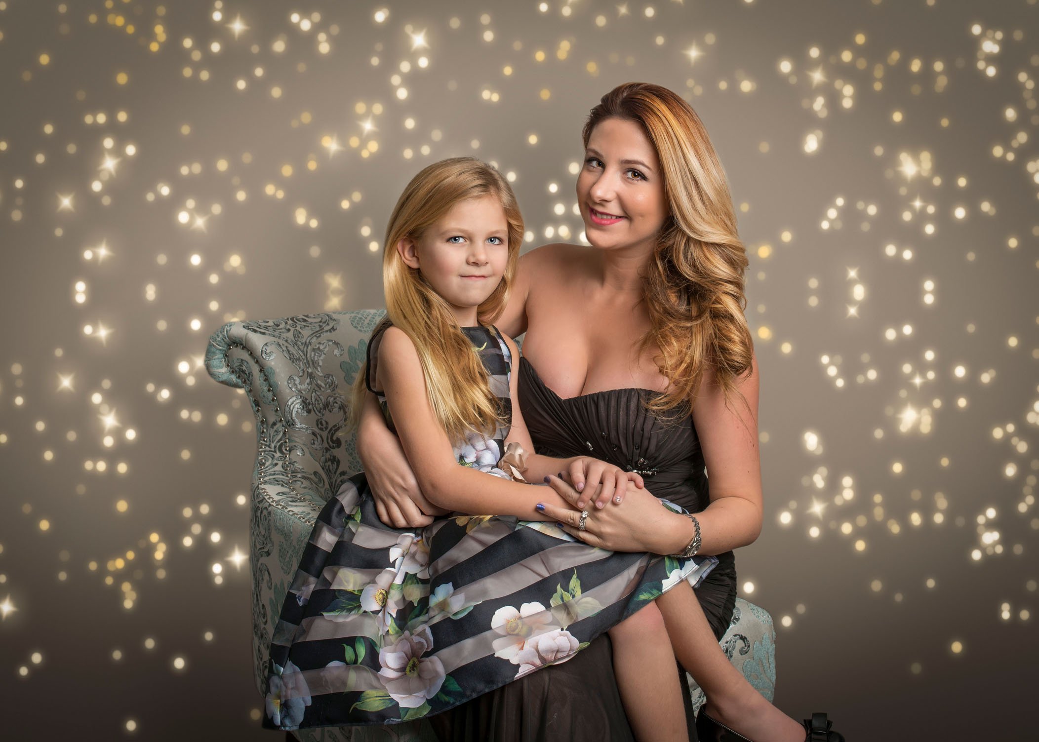 Mom seated with 7 year old daughter sitting on her lap with bokeh lights