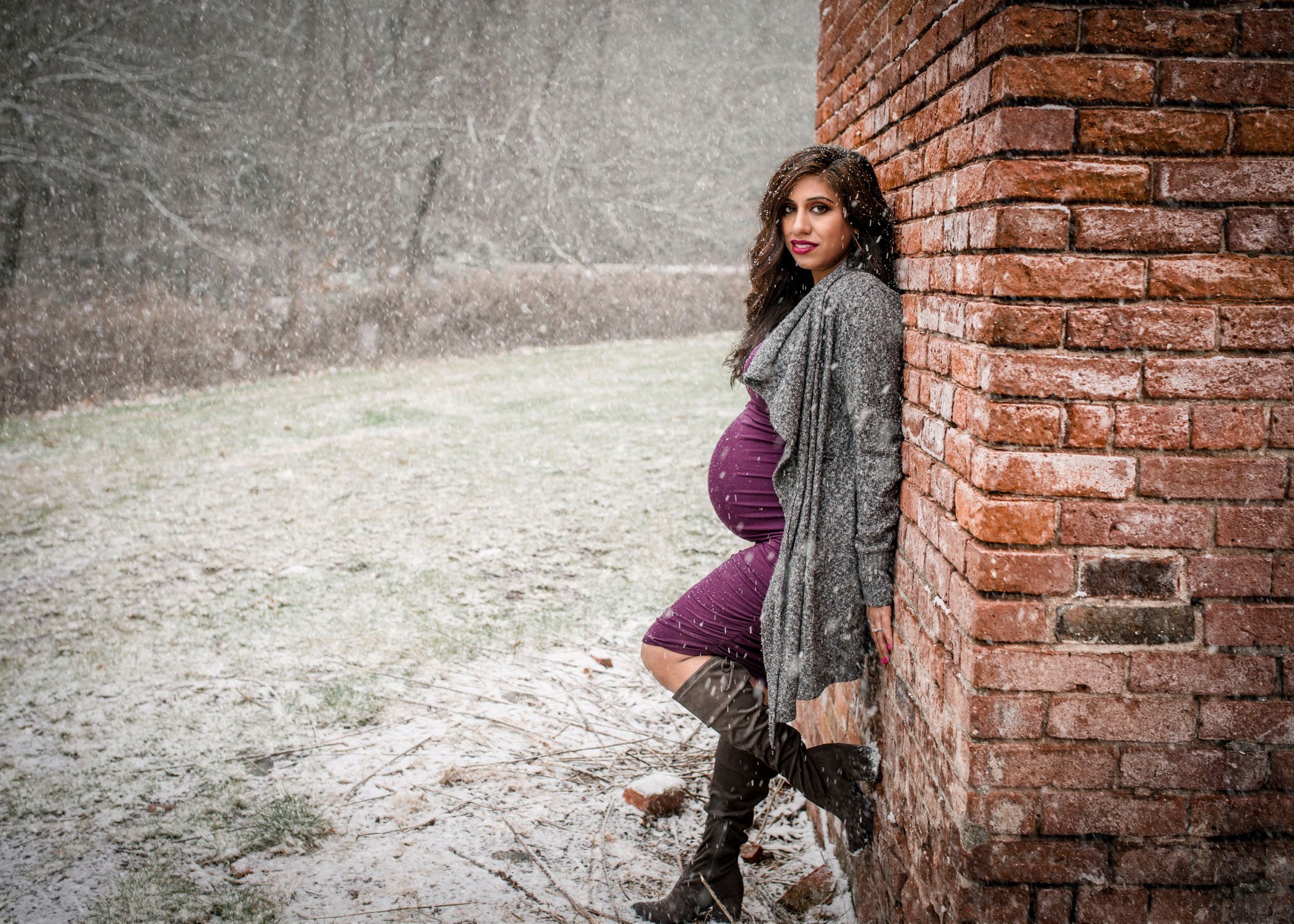pregnant Indian woman leaning against brick wall outside in the snow