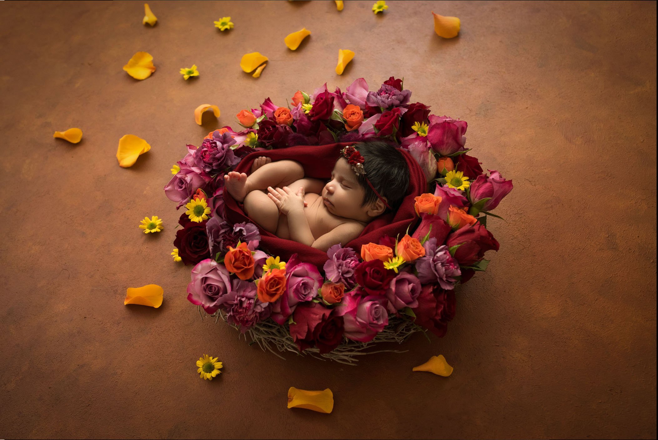 newborn baby girl sleeping in next of pink, red and orange roses