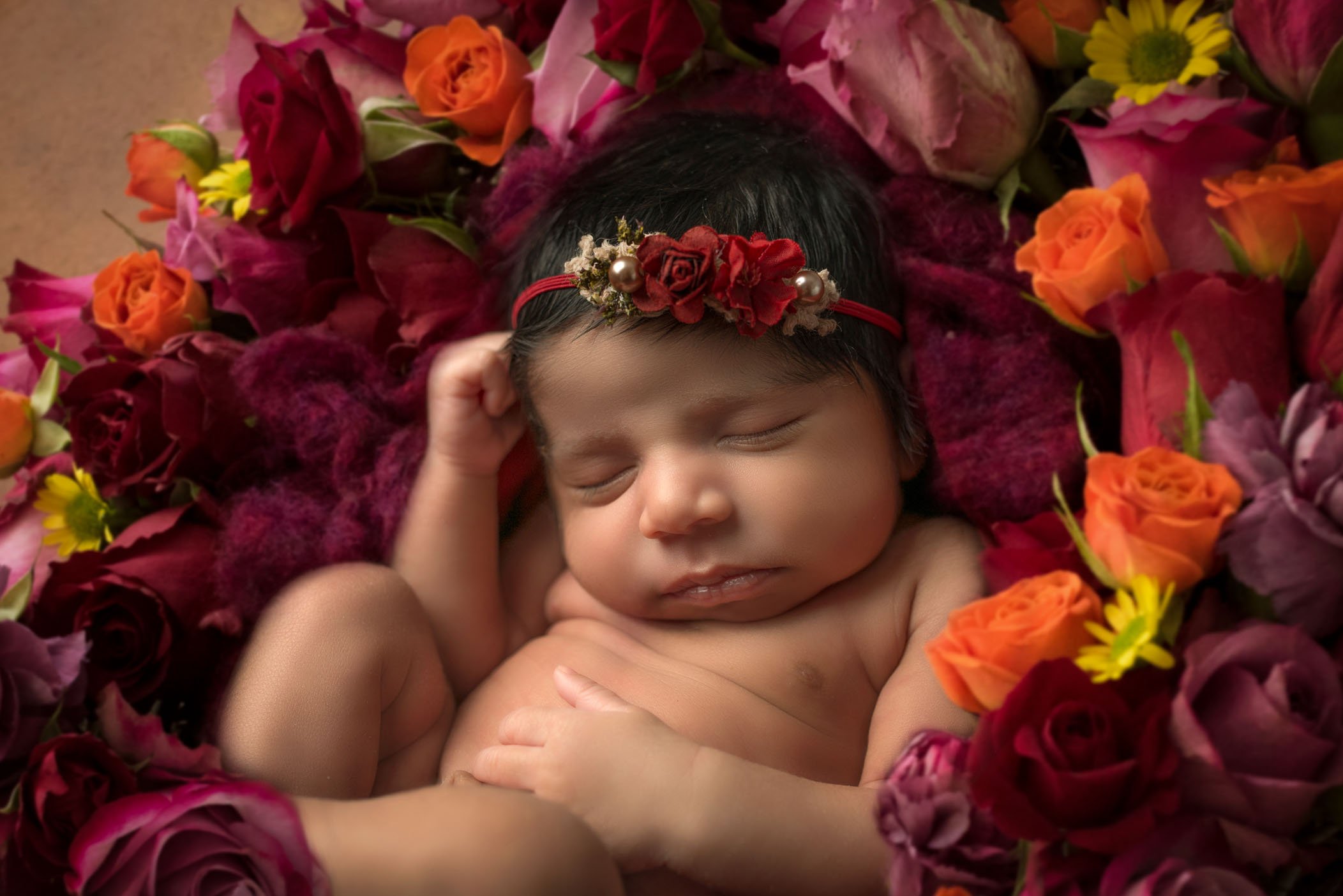 close up of newborn baby girl sleeping in bed of red and orange roses