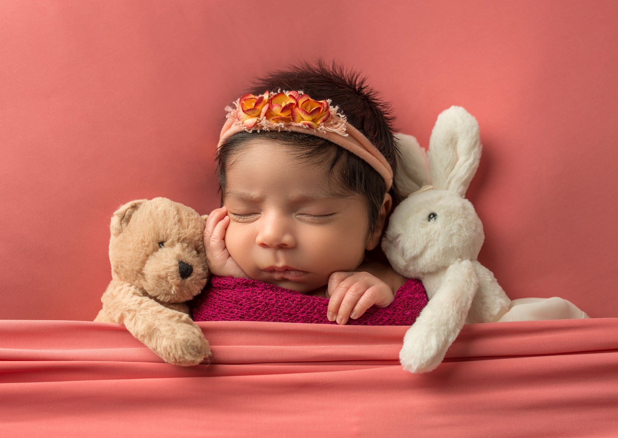 newborn baby girl sleeping with bunny and bear on coral background