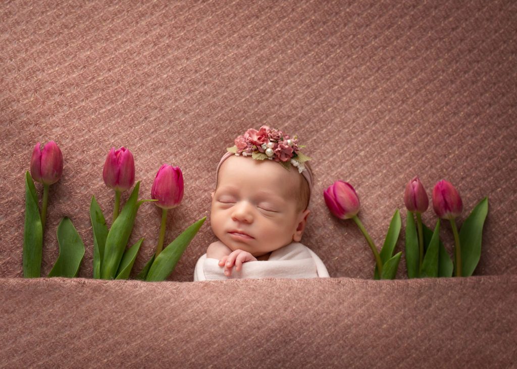 newborn baby sleeping in pink bed with bright pink tulips next to her