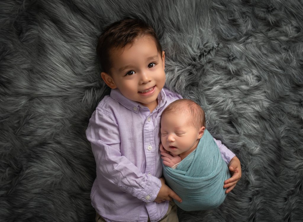 Toddler boy holding his brand new newborn brother