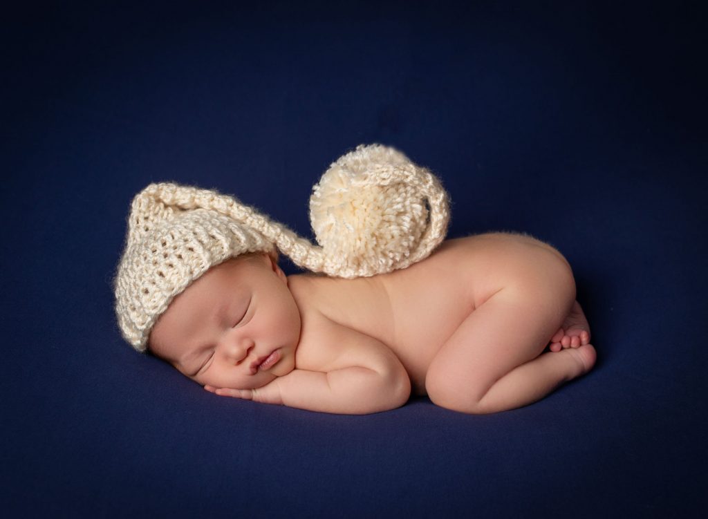newborn baby sleeping with a curled knit hat on a dark blue background
