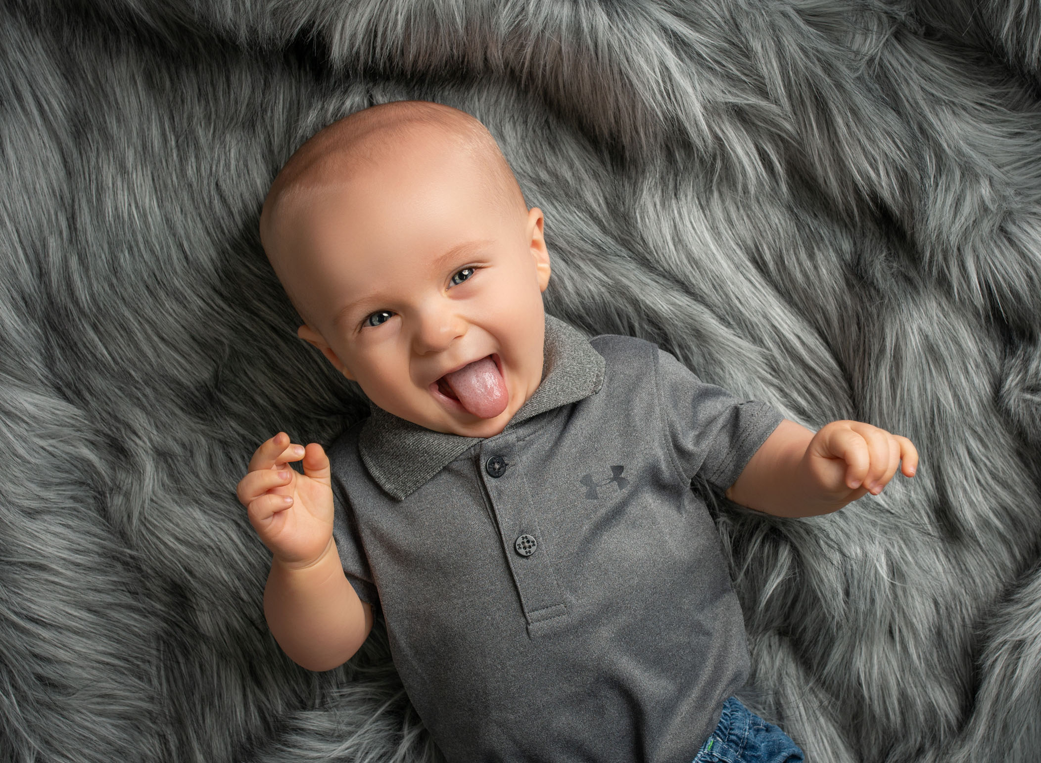 6 month old baby boy sticking his tongue out and smiling on grey fur blanket