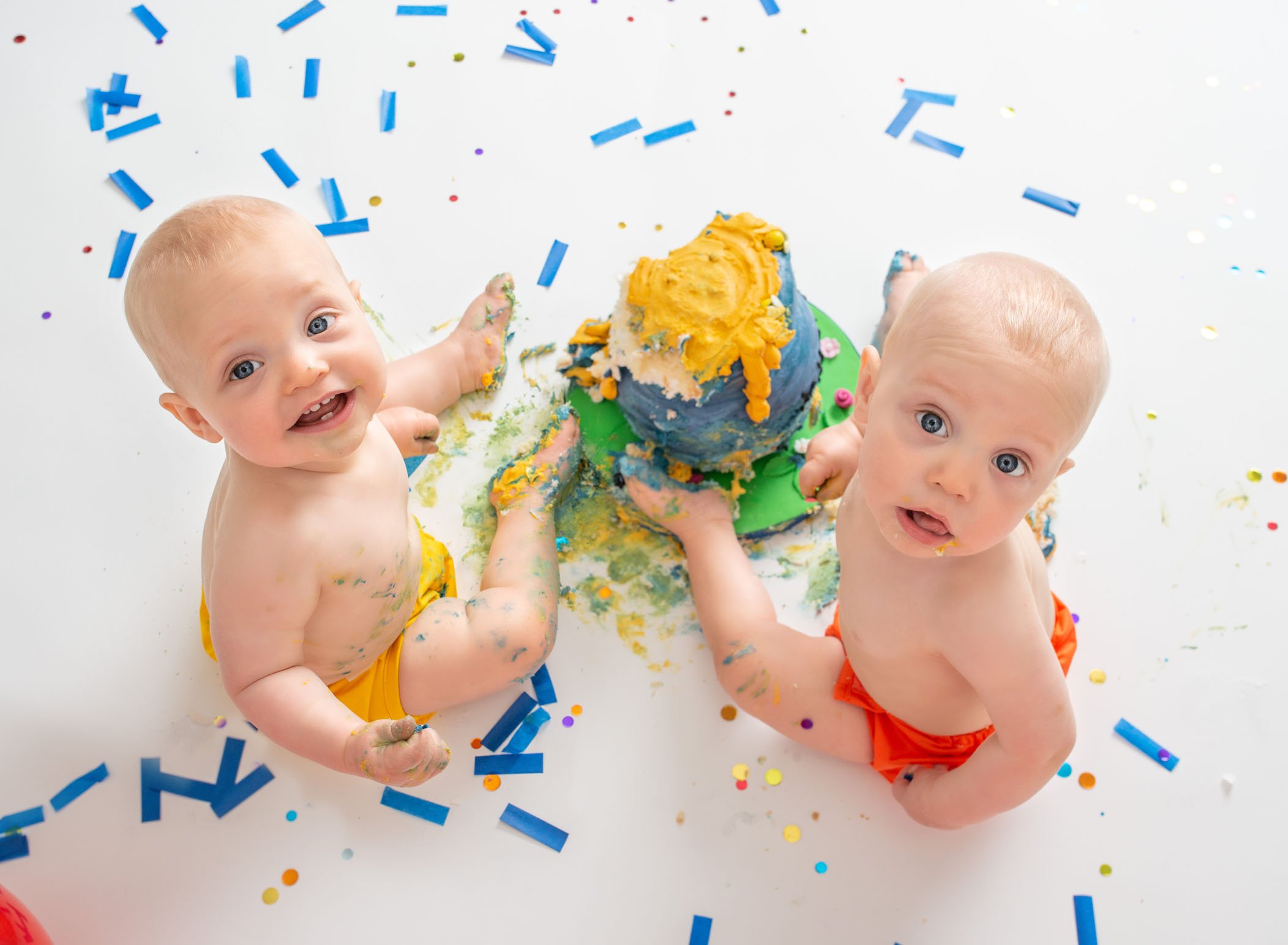 Twin one year old boys look up from their smashed cake