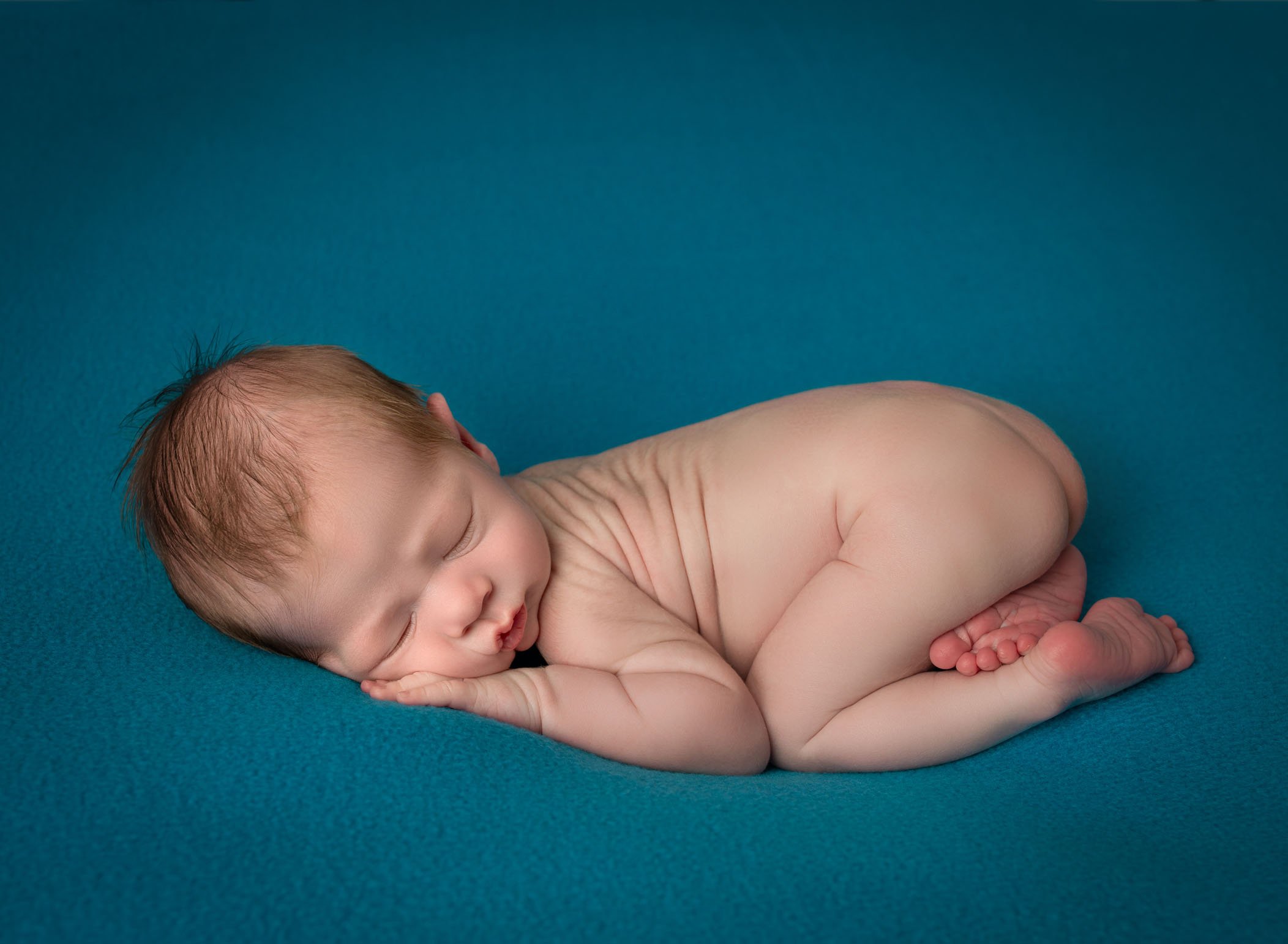 newborn baby boy sleeping in bum up position on teal blanket